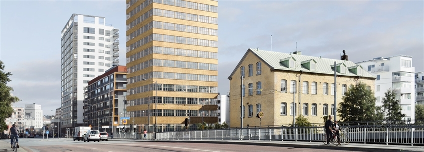 Om projektet - Ett höghus i industriell design i rad med mindre och större fastigheter längs en bilväg. 