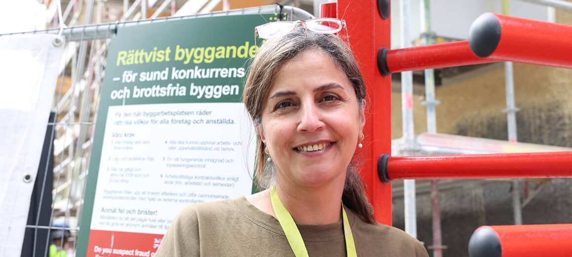Projektledare Payam Hakemivala står framför ett byggstaket med Rättvist byggande-skylt.